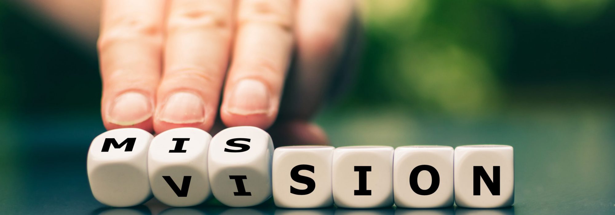 From a vision to a mission. Hand turns dice and changes the word vision to mission.